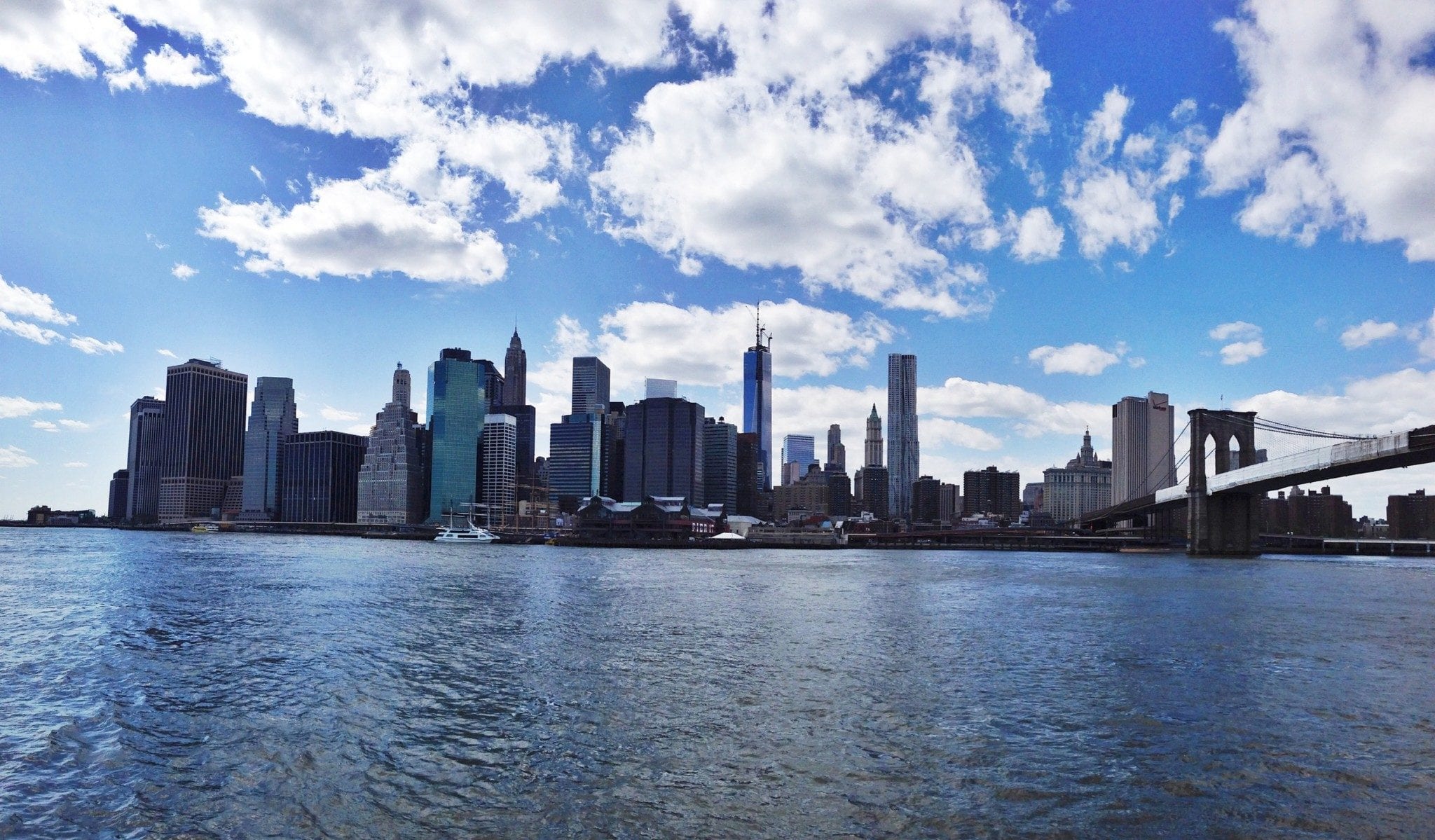 View of the New York City Skyline with puffy white clouds in a blue sky.