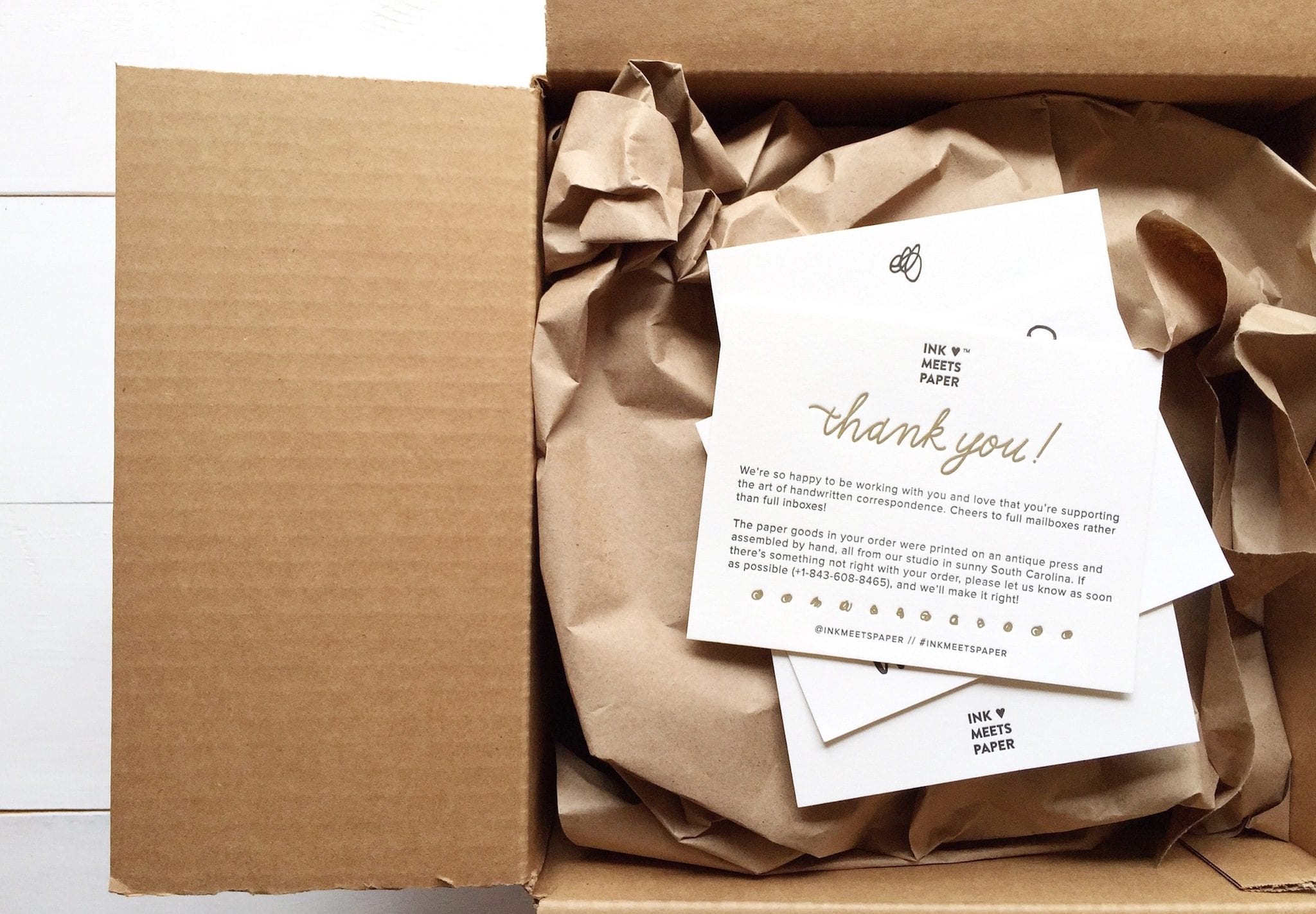 Open shipping box with brown paper stuffing and company printed collateral
