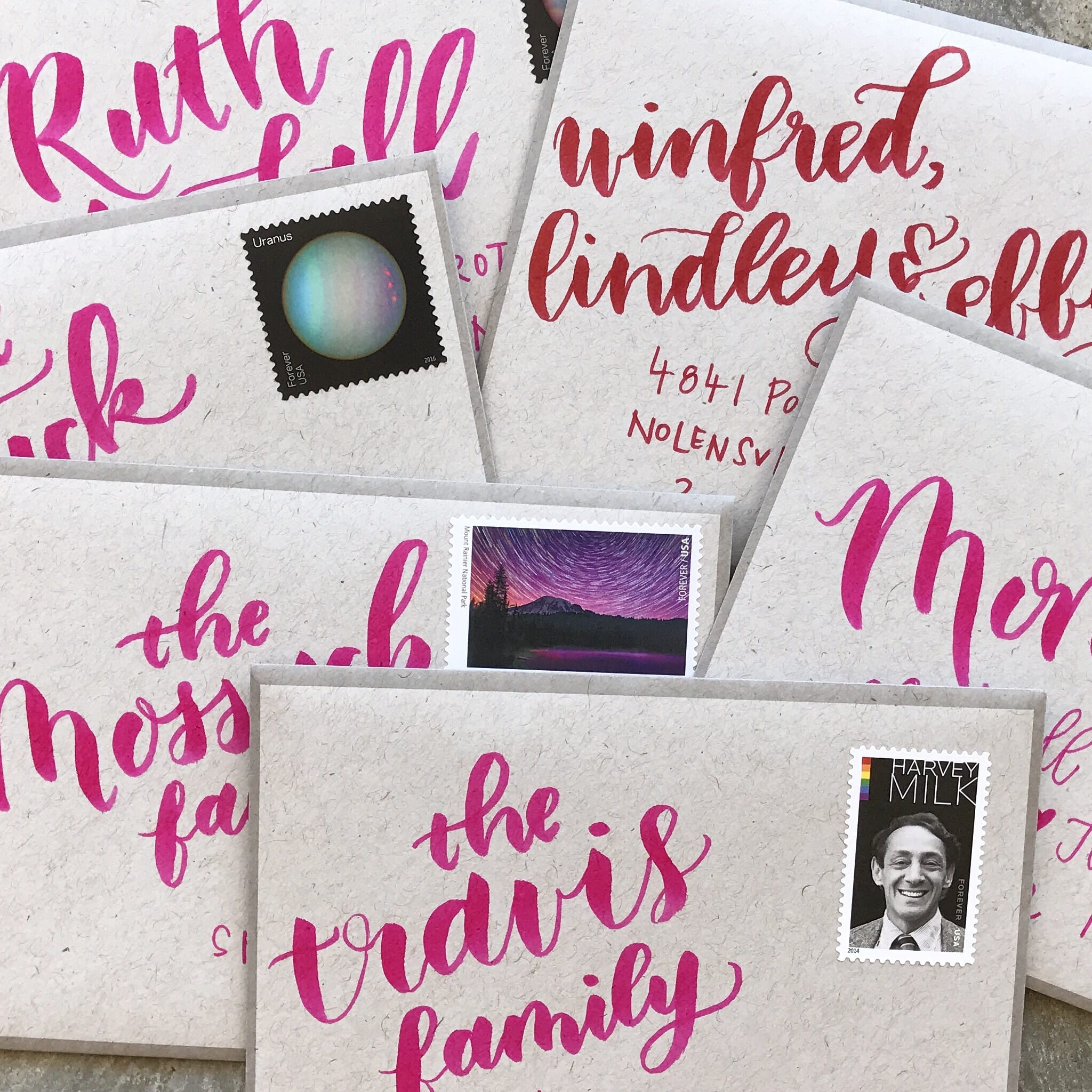 Hot pink brushed lettering on envelopes in a pile.