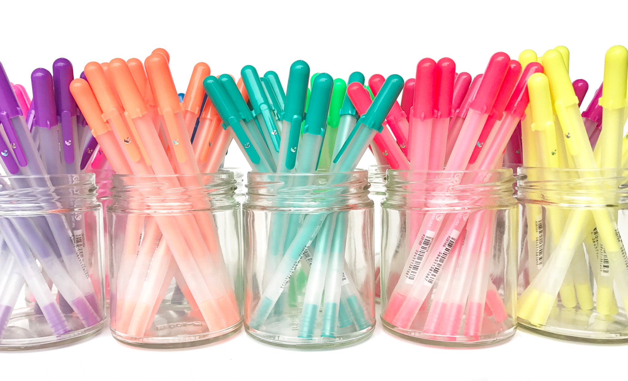 Colored gel pens organized in glass containers on white background