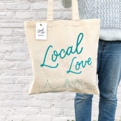 Model wearing market bag over shoulder. Bag shows handlettered words Local Love and a line drawing of the skyline of Charleston, SC