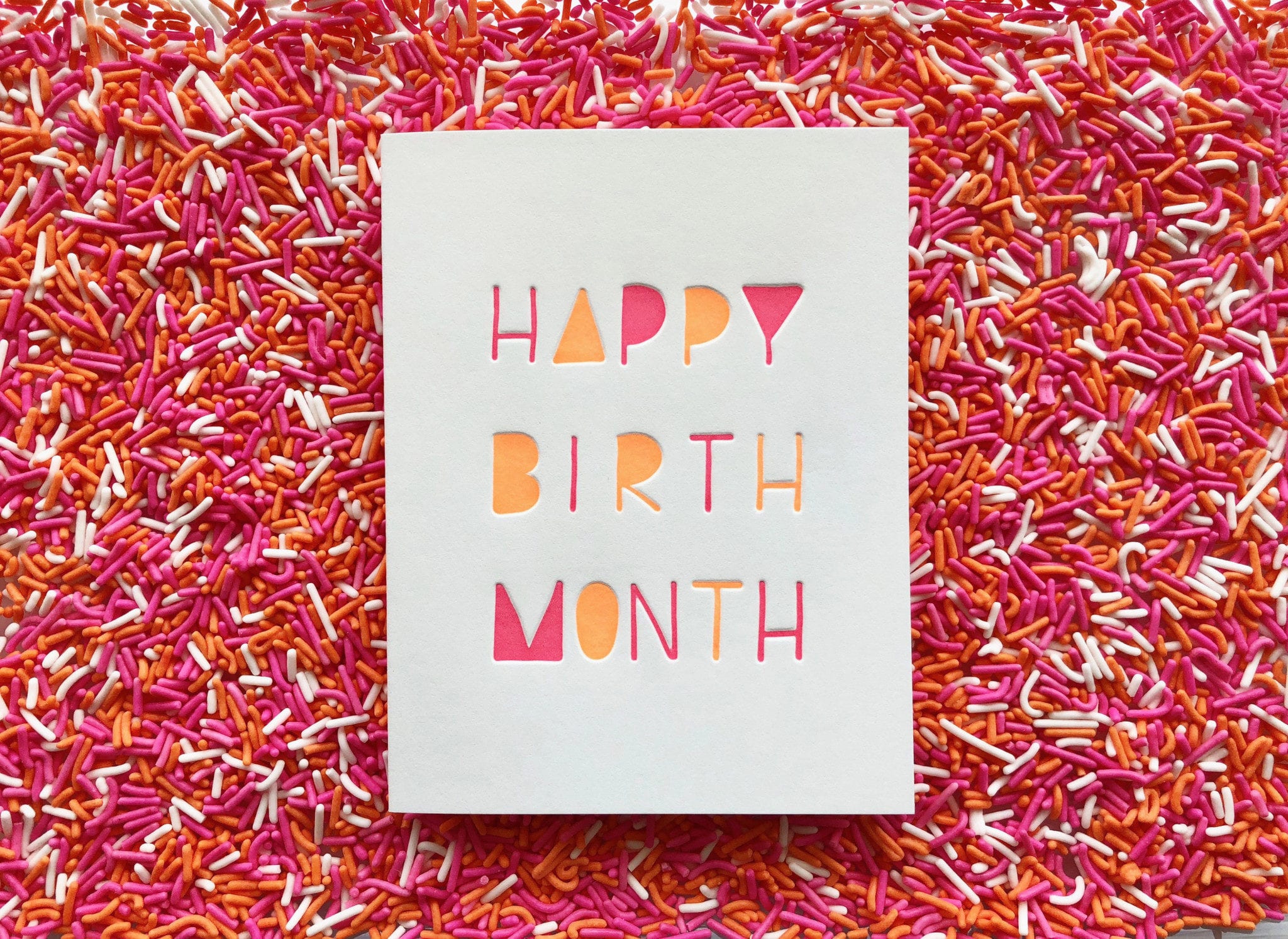 card reading happy birth month on a bed of red colored sprinkles
