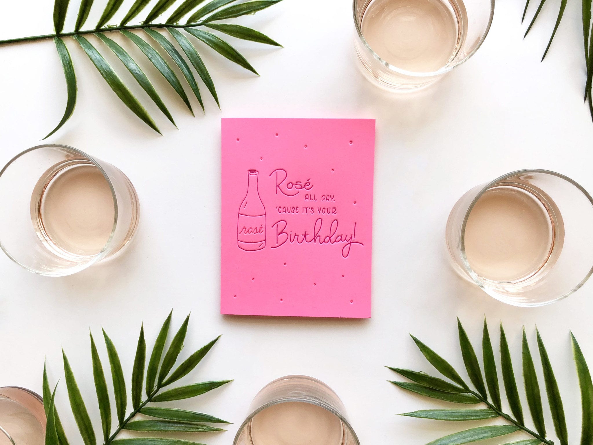 hot pink greeting card arranged with glasses of rosé and palm leaves